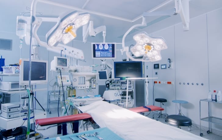病院の施術室の写真。大きなアームライトや、医療モニターとケーブルで繋がった医療用機具が写っている